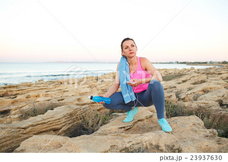 Woman sitting after morning running on the rocks by the sea Woman sitting after morning running on the rocks by the sea 23937630
