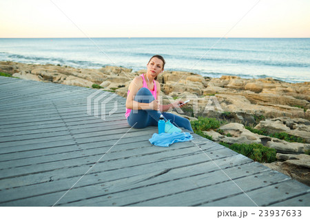 Woman resting after jogging on a wooden path at the sea 23937633