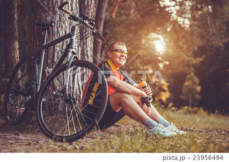Cyclist resting under a tree and drinking water 23956494