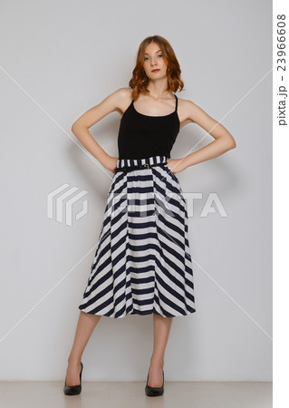 Pretty girl in skirt posing near white wall. Female legs in black shoes. Stript 23966608