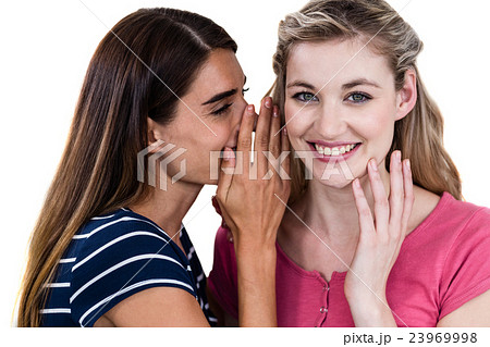 Smiling woman telling secret to friend while standing 23969998