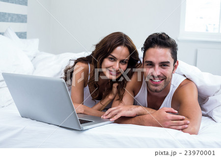 Portrait of smiling couple with laptop while lying under blanket Portrait of smiling couple with laptop while lying under blanket 23970001