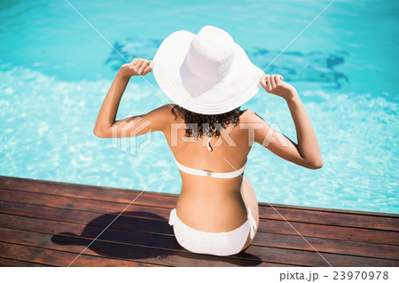 Rear view of woman wearing white bikini and hat sitting near poo Rear view of woman wearing white bikini and hat sitting near poo 23970978