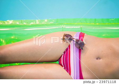 Mid section of a woman in bikini lying on air bed with sunglasse Mid section of a woman in bikini lying on air bed with sunglasse 23971118