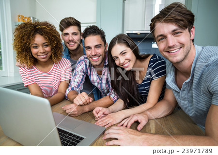 Multi-ethnic friends smiling while using laptop on table 23971789