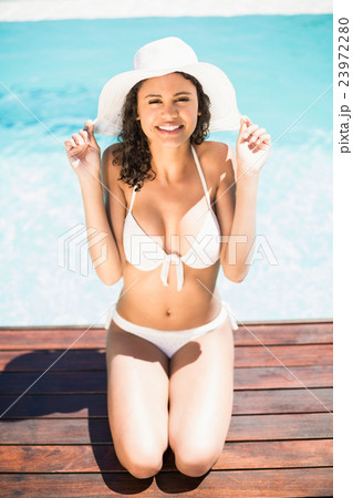 Happy woman in hat sitting by pool side 23972280