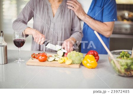 Midsection of senior man standing with woman cutting salad 23972485