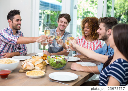 Young friends toasting wine while having meal at table Young friends toasting wine while having meal at table 23972757