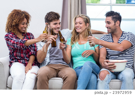 Multi-ethnic friends toasting beer while sitting on sofa 23972959