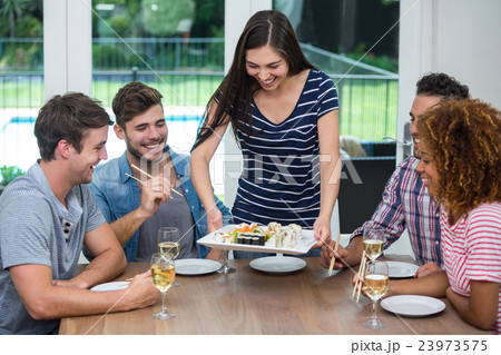 Woman serving sushi to friends while drinking wine Woman serving sushi to friends while drinking wine 23973575