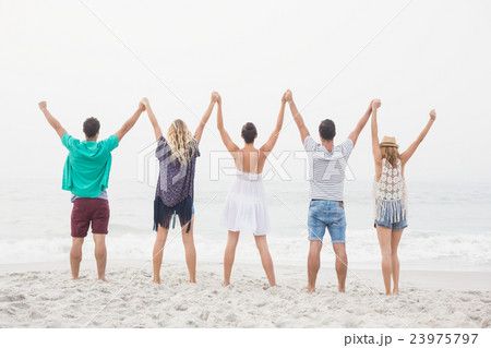 Rear view of friends holding hands and standing in a row 23975797