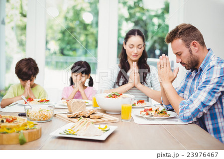 Family praying while sitting at dining table Family praying while sitting at dining table 23976467