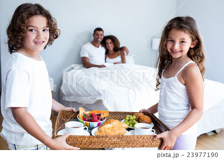 Portrait of daughter and son carrying breakfast tray for parents 23977190