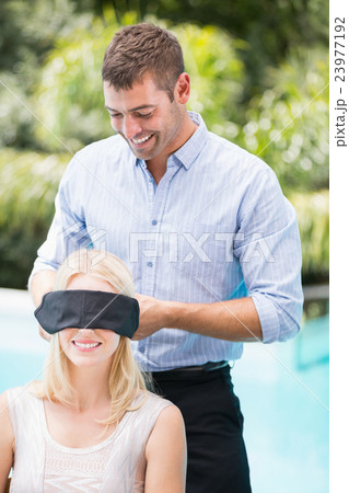 Smiling man blindfolding woman 23977192