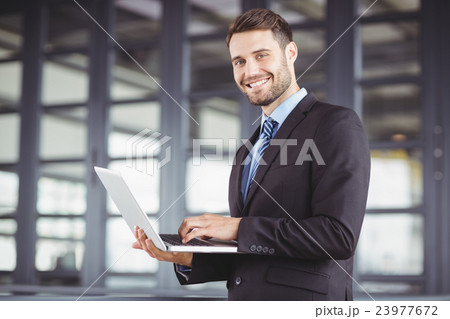 Handsome businessman smiling while using laptop 23977672