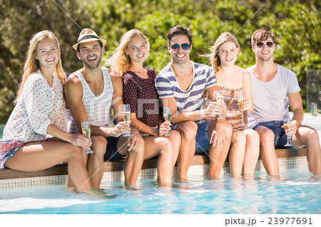 Group of friends sitting at poolside with glass of champagne Group of friends sitting at poolside with glass of champagne 23977691