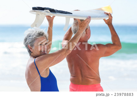 Cute mature couple holding a surfboard Cute mature couple holding a surfboard 23978883