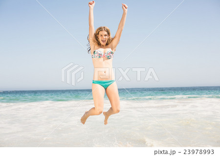Carefree woman in bikini jumping on the beach Carefree woman in bikini jumping on the beach 23978993