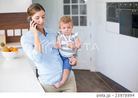 Woman talking on mobile phone while carrying daughter 23978994