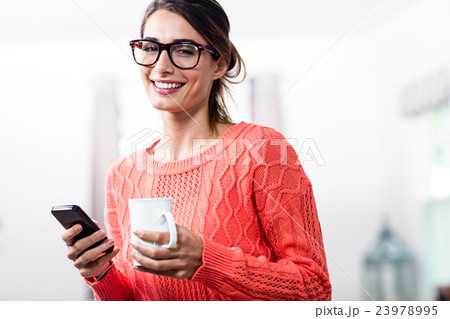 Happy young woman with mobile phone and mug Happy young woman with mobile phone and mug 23978995
