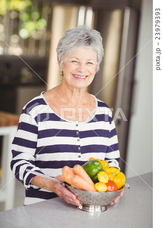 Portrait of cheerful senior woman holding colander with vegetabl 23979393