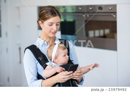 Woman using mobile phone while carrying baby girl 23979492