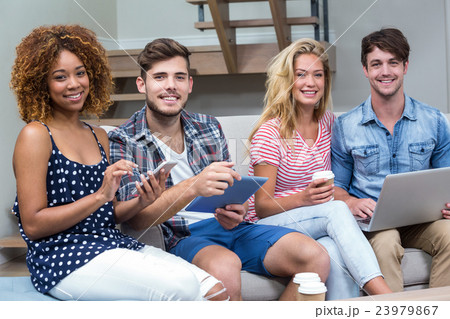 Friends smiling while using technologies on sofa Friends smiling while using technologies on sofa 23979867