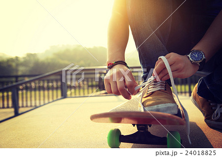 skateboarder tying shoelace at skatepark ramp 24018825