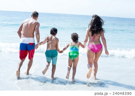 Rear view of family running towards sea Rear view of family running towards sea 24048390