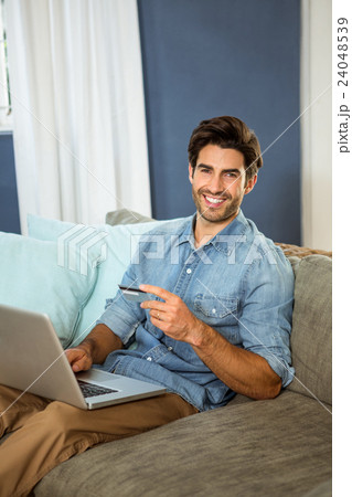 Portrait of young man sitting on sofa and shopping online on laptop Portrait of young man sitting on sofa and shopping online on laptop 24048539