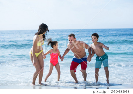 Family in swimwear holding hands while enjoying 24048643