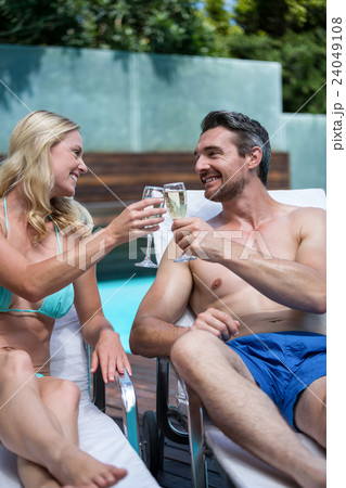 Couple sitting on sun lounger and toasting champagne glass 24049108