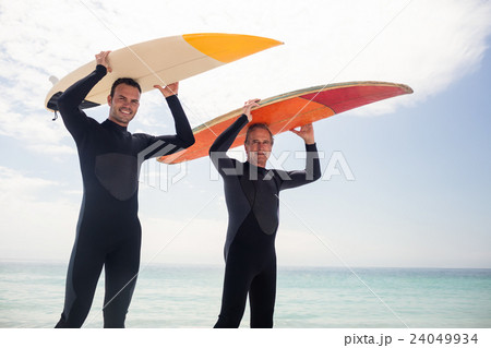 Portrait of happy father and son carrying a surfboard over their head 24049934