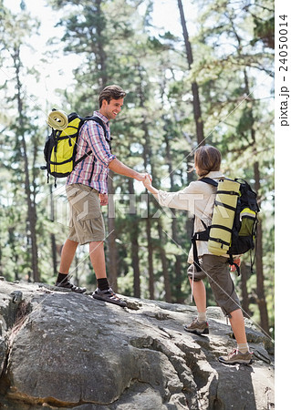 Man helping woman climb rock in forest Man helping woman climb rock in forest 24050014