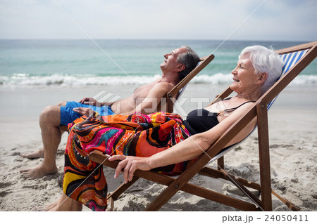 Happy senior couple relaxing on deckchairs at beach 24050411