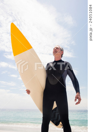Senior man in wetsuit holding a surfboard 24051084