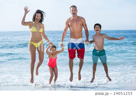 Family in swimwear jumping at sea shore Family in swimwear jumping at sea shore 24051255