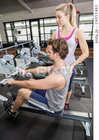 Female trainer assisting a man on rowing machine 24051461