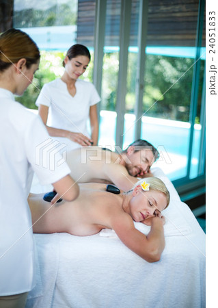 Young couple receiving a hot stone massage from masseur Young couple receiving a hot stone massage from masseur 24051833