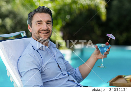 Smart man holding martini glass while relaxing in sun lounger Smart man holding martini glass while relaxing in sun lounger 24052134