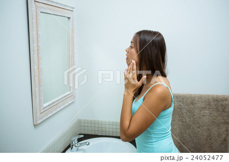 Woman checking her skin in bathroom Woman checking her skin in bathroom 24052477