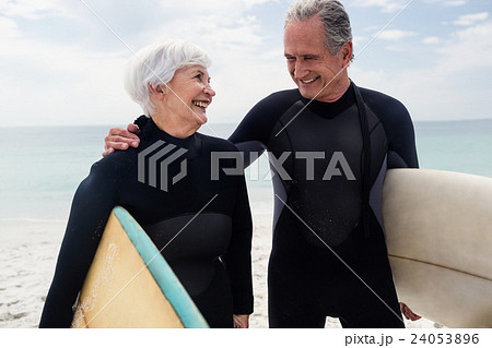 Senior couple in wetsuit holding surfboard on beach  24053896