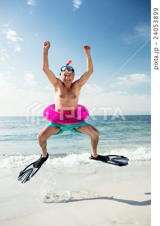 Happy senior man in inflatable ring and flippers jumping on beach Happy senior man in inflatable ring and flippers jumping on beach 24053899