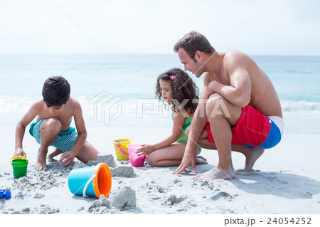 Father helping children building sand castle at beach Father helping children building sand castle at beach 24054252