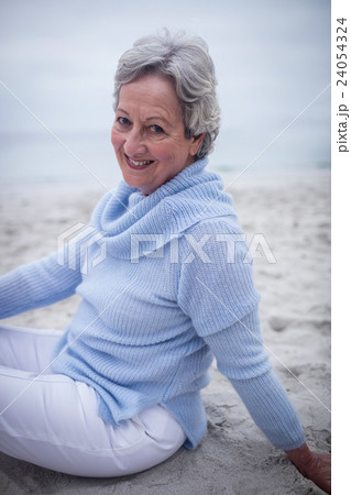 Portrait of happy senior woman sitting on beach 24054324