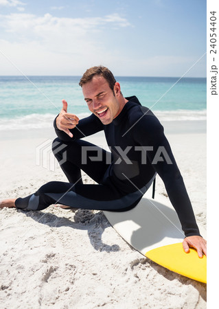 Happy surfer in wetsuit sitting with surfboard on the beach 24054404