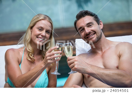 Couple sitting on sun lounger toasting champagne 24054501