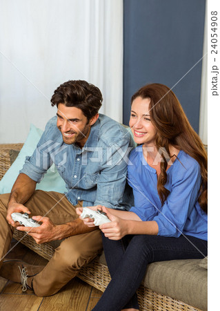 Young couple playing video game while sitting on sofa Young couple playing video game while sitting on sofa 24054908