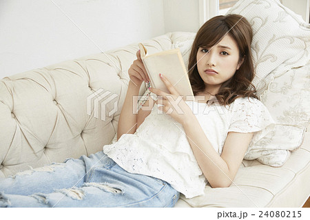 ソファに横になり読書する若い女性 24080215