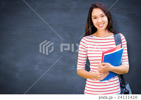 Composite image of college girl holding books with blurred students in park 24111420